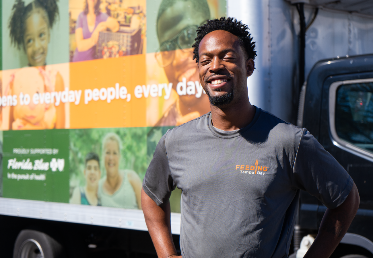 Ryan, smiling and wearing a Feeding Tampa Bay shirt in front of one of the delivery trucks.